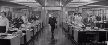 Movie still from “One, Two, Three” (1961), directed by Billy Wilder – A man in a suit and tie walking down a hall way; Wide shot, Over the shoulder angle