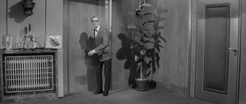 Movie still from “One, Two, Three” (1961), directed by Billy Wilder – A man in a suit standing next to a plant; Wide shot, Low angle