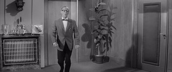 Movie still from “One, Two, Three” (1961), directed by Billy Wilder – A man in a suit and bow tie standing in front of a plant; Wide shot, Low angle