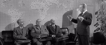 Movie still from “One, Two, Three” (1961), directed by Billy Wilder – A man taking a picture of two men in suits; Medium shot, High angle