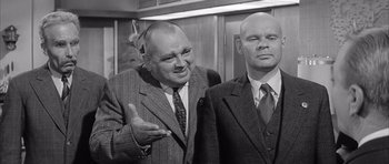 Movie still from “One, Two, Three” (1961), directed by Billy Wilder – Two men standing next to each other in front of an elevator; Medium shot, Over the shoulder angle