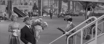 Movie still from “One, Two, Three” (1961), directed by Billy Wilder – An old black and white photo of a woman holding flowers; Wide shot, Over the shoulder angle