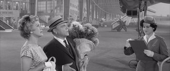 Movie still from “One, Two, Three” (1961), directed by Billy Wilder – A black and white photo of a man holding a bouquet of flowers; Medium shot, Over the shoulder angle