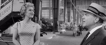 Movie still from “One, Two, Three” (1961), directed by Billy Wilder – An old photo of a woman standing in front of a building; Medium shot, Over the shoulder angle