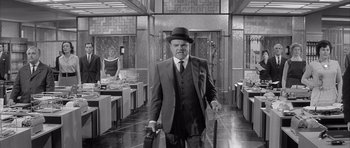Movie still from “One, Two, Three” (1961), directed by Billy Wilder – An older man in a suit and hat holding a cane; Wide shot, Low angle