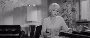 Movie still from “One, Two, Three” (1961), directed by Billy Wilder – A black and white photo of a woman writing on a piece of paper; Medium shot, High angle