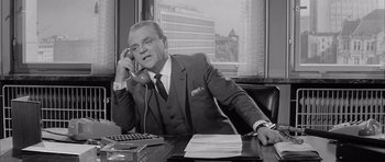 Movie still from “One, Two, Three” (1961), directed by Billy Wilder – An older man sitting at a desk talking on a phone; Medium shot, Low angle