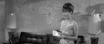 Movie still from “One, Two, Three” (1961), directed by Billy Wilder – A woman holding a book in front of a map of the world; Medium shot, Over the shoulder angle