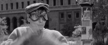 Movie still from “One, Two, Three” (1961), directed by Billy Wilder – A man wearing glasses and a hat is standing in front of a building; Close Up shot, Over the shoulder angle