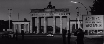 Movie still from “One, Two, Three” (1961), directed by Billy Wilder – Two men standing in front of a building with a statue on top of it; Extreme Wide shot, Low angle