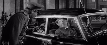 Movie still from “One, Two, Three” (1961), directed by Billy Wilder – An old photo of a man sitting in the back of a car; Medium shot, Over the shoulder angle