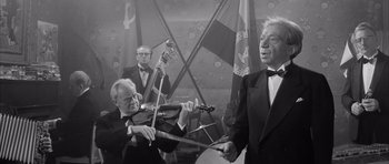 Movie still from “One, Two, Three” (1961), directed by Billy Wilder – A group of men playing musical instruments in front of a flag; Medium shot, Low angle