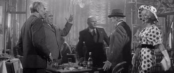 Movie still from “One, Two, Three” (1961), directed by Billy Wilder – A group of men standing around a table with drinks; Medium shot, Over the shoulder angle