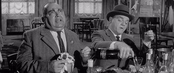 Movie still from “One, Two, Three” (1961), directed by Billy Wilder – Two men sitting at a table in front of a bottle of wine; Medium shot, High angle