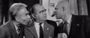 Movie still from “One, Two, Three” (1961), directed by Billy Wilder – A man in a suit and tie talking to two other men; Close Up shot, Low angle