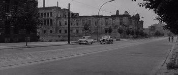 Movie still from “One, Two, Three” (1961), directed by Billy Wilder – Two cars are driving down the street in a black and white photo; Extreme Wide shot, Low angle