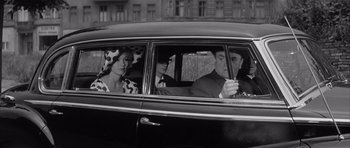 Movie still from “One, Two, Three” (1961), directed by Billy Wilder – A black and white photo of a man and two women sitting in the back of a car; Medium shot, Over the shoulder angle
