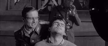 Movie still from “One, Two, Three” (1961), directed by Billy Wilder – A man is getting his head shaved by two other men in military uniforms; Medium shot, High angle