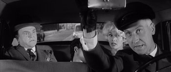 Movie still from “One, Two, Three” (1961), directed by Billy Wilder – A man and a woman riding in the back of a car; Medium shot, Over the shoulder angle