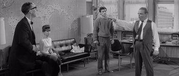 Movie still from “One, Two, Three” (1961), directed by Billy Wilder – A man in a room with a chair and a couch; Medium shot, Over the shoulder angle