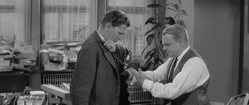 Movie still from “One, Two, Three” (1961), directed by Billy Wilder – A man in a suit and tie cutting another man's tie with a pair of scissors; Medium shot, Over the shoulder angle