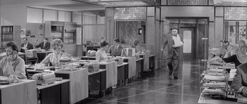 Movie still from “One, Two, Three” (1961), directed by Billy Wilder – A group of people sitting at tables in a room; Wide shot, High angle