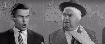 Movie still from “One, Two, Three” (1961), directed by Billy Wilder – A man in a suit and a hat standing next to another man in a suit; Close Up shot, Over the shoulder angle