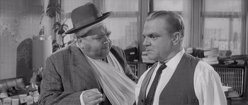 Movie still from “One, Two, Three” (1961), directed by Billy Wilder – Two men in suits and hats one of which has a tie around his neck; Medium shot, Over the shoulder angle