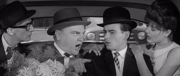 Movie still from “One, Two, Three” (1961), directed by Billy Wilder – Two men in hats and ties are in a car; Close Up shot, Over the shoulder angle