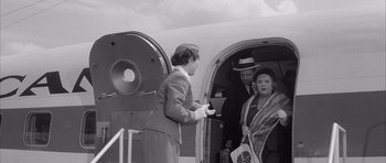 Movie still from “One, Two, Three” (1961), directed by Billy Wilder – An old black and white photo of a woman getting into an airplane; Wide shot, High angle