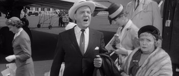 Movie still from “One, Two, Three” (1961), directed by Billy Wilder – An older man wearing a suit and hat while holding a jacket; Medium shot, Low angle