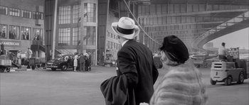 Movie still from “One, Two, Three” (1961), directed by Billy Wilder – A man wearing a hat and a suit walking down a street; Wide shot, Over the shoulder angle