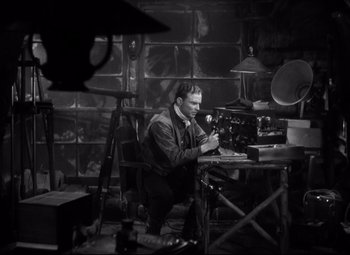 Movie still from “Only Angels Have Wings” (1939), directed by Howard Hawks – A black and white photo of a man sitting at a desk; Medium shot, High angle