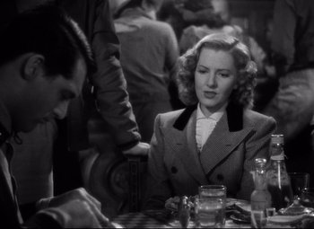 Movie still from “Only Angels Have Wings” (1939), directed by Howard Hawks – A woman sitting at a table with a man in the background; Medium shot, High angle