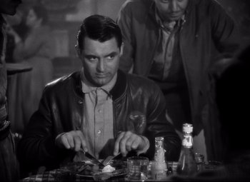 Movie still from “Only Angels Have Wings” (1939), directed by Howard Hawks – A man sitting at a table with a plate in front of him; Medium shot, Over the shoulder angle