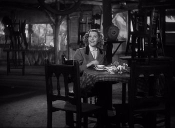 Movie still from “Only Angels Have Wings” (1939), directed by Howard Hawks – A black and white photo of a woman sitting at a table; Wide shot, High angle