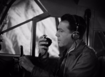 Movie still from “Only Angels Have Wings” (1939), directed by Howard Hawks – A black and white photo of a man wearing headphones and using a cell phone; Close Up shot, High angle