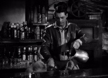 Movie still from “Only Angels Have Wings” (1939), directed by Howard Hawks – A black and white photo of a man pouring a drink; Medium shot, High angle