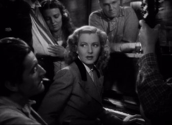 Movie still from “Only Angels Have Wings” (1939), directed by Howard Hawks – A woman in a suit and tie sitting at a piano; Medium shot, High angle