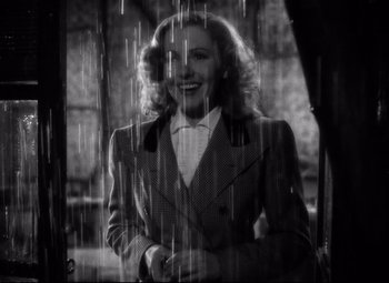 Movie still from “Only Angels Have Wings” (1939), directed by Howard Hawks – A black - and - white photo of a woman standing in the rain; Medium shot, Low angle