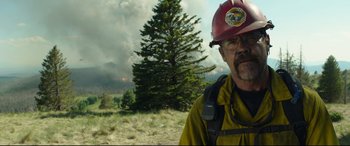 Movie still from “Only the Brave” (2017), directed by Joseph Kosinski – A man wearing a red hat standing in front of a tree; Medium shot, Over the shoulder angle