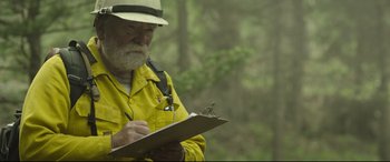 Movie still from “Only the Brave” (2017), directed by Joseph Kosinski – An older man in a yellow shirt writing on a clipboard; Close Up shot, Over the shoulder angle