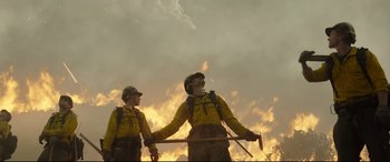 Movie still from “Only the Brave” (2017), directed by Joseph Kosinski – A couple of men standing next to each other on top of a field; Medium shot, Low angle