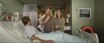 Movie still from “Only the Brave” (2017), directed by Joseph Kosinski – Two women and a baby standing next to a man in a hospital bed; Wide shot, High angle