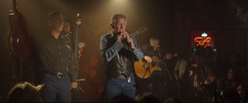 Movie still from “Only the Brave” (2017), directed by Joseph Kosinski – An older man plays a flute while a man plays a guitar and another man plays a guitar; Wide shot, Low angle