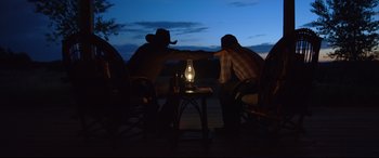 Movie still from “Only the Brave” (2017), directed by Joseph Kosinski – Two men sitting at a table with a lit lamp; Wide shot, Over the shoulder angle