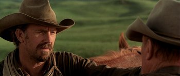 Movie still from “Open Range” (2003), directed by Kevin Costner – A man wearing a cowboy hat is riding a horse; Close Up shot, Over the shoulder angle