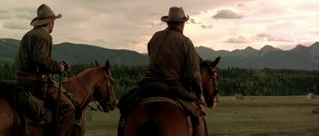 Movie still from “Open Range” (2003), directed by Kevin Costner – A man riding on the back of a brown horse; Wide shot, Low angle