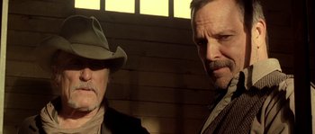 Movie still from “Open Range” (2003), directed by Kevin Costner – Two men standing next to each other near a wooden wall; Close Up shot, Low angle