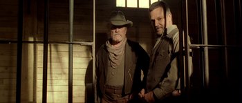 Movie still from “Open Range” (2003), directed by Kevin Costner – Two men standing next to each other in a room; Medium shot, Low angle